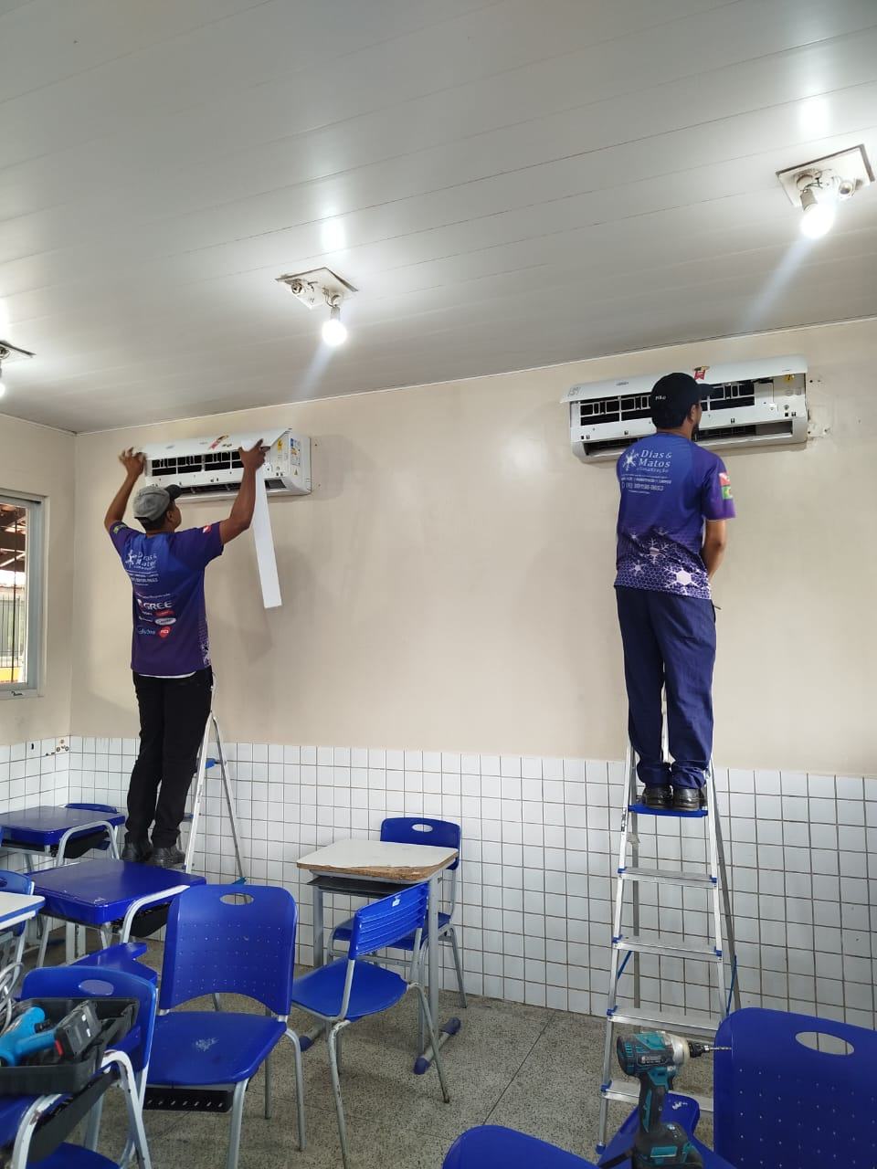 Dois técnicos uniformizados da Dias & Matos realizando serviço em aparelhos de ar-condicionado split em uma sala